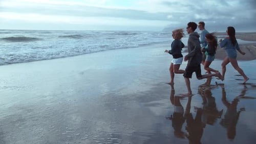 Young friends run together in super slow motion to the beach for summer vacation