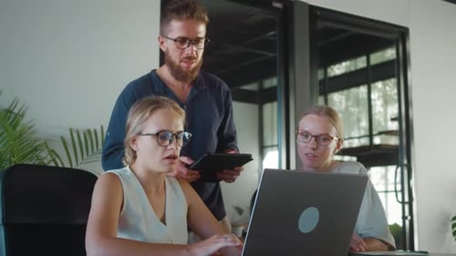Office Workers Collaborating on Project Utilizing Laptop and Tablet While Male Manager Oversees