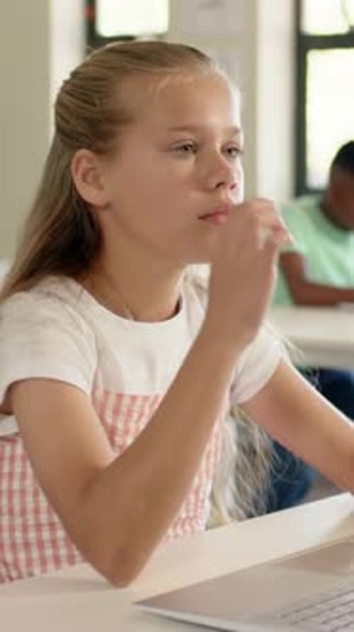 Vertical video: Blinking girl in pink dress shifting laptop work into thinking chin pose in class