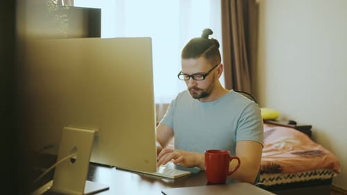 A Young Guy Works Remotely Sitting at a Table and Writes Notes on a Computer