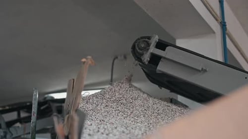 rubber granules pouring from conveyor into container at recycling plant