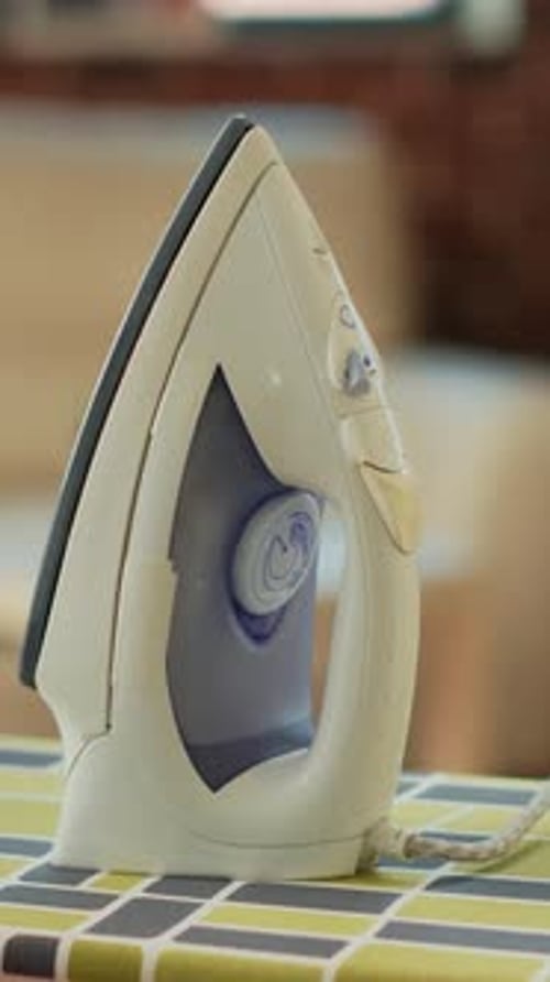 Vertical Video Iron Tool Placed on Ironing Board with Pile of Washed Clothing