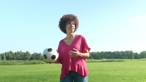 Attractive femme afro-américaine positive jonglant avec le ballon de football en plein air