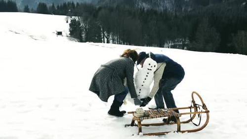 Woman and man build snowman on snowy hill