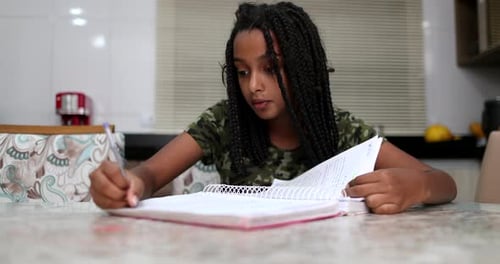 Girl Studying at Table Indoors, Writing in Notebook