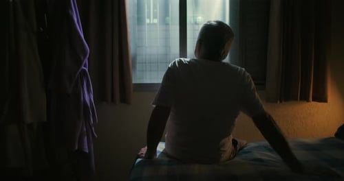 Senior Man Sitting on Bed Gazing out Window