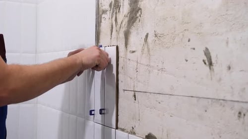 Hands Carefully Apply White Tile to Wall