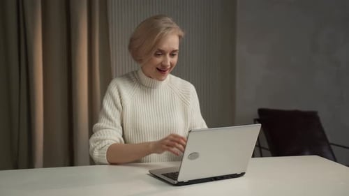 Joyful Woman Celebrating Success at Her Desk With Arms Raised in Triumph