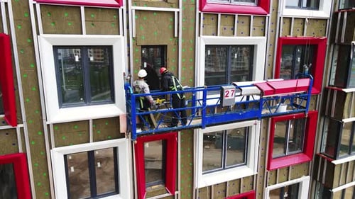 Workers in a Cradle Install the Window Trim of a Multi-storey Building under Construction
