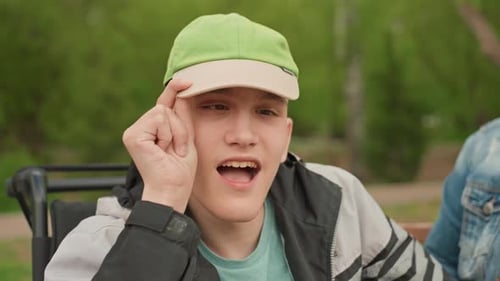 Young White Man In Wheelchair Laughing With Caregiver On Bench Bright Smile Closeup Emotion Spring