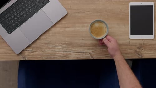 Blick von oben nach unten auf die Kaffeetasse, die auf dem Tisch neben Laptop und Tablet steht, Arbeitstage im Büro oder