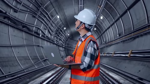 Side View Of Asian Male Engineer Working On A Laptop In Subway Tunnel