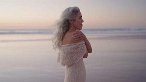Serene Senior Woman with Silver Hair Stands on Beach at Sunset Embracing the Moment of Peace