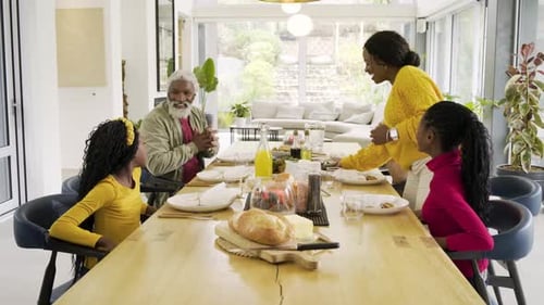 When Black mother entering with tray, diverse family placing dishes at dining table prepping meal