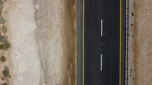 Aerial static close-up drone shot of a white car passing fast on a road in the middle of an Israeli
