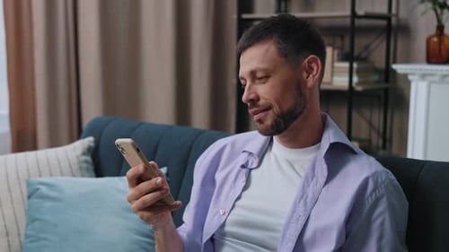 Man Using Smartphone Relaxing on Sofa at Home