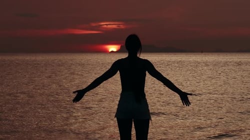 Silhouette of Woman Looks at Sun Disk on Sky During Red Sunset on the Sea Before Sun Goes Below