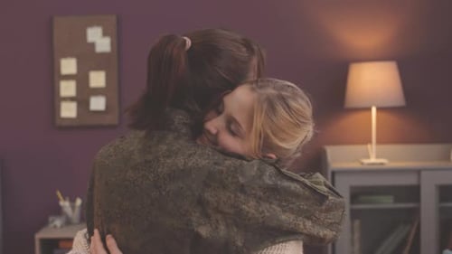 Soldier Hugs Child Holding American Flag in Home