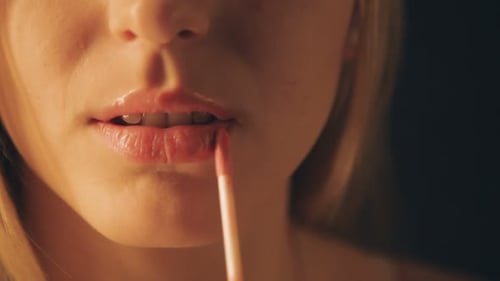 Beautiful young woman paints her sexy lips with red lipstick on black background