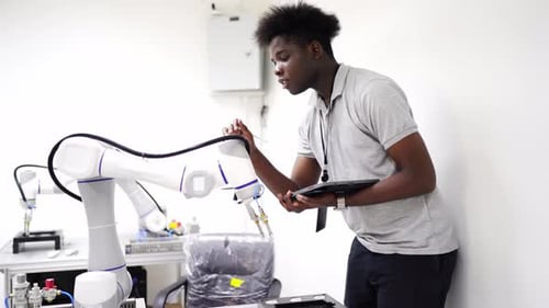 Robotics engineer fitting sensors to traditional engineering Robot Arm in robotics research facility
