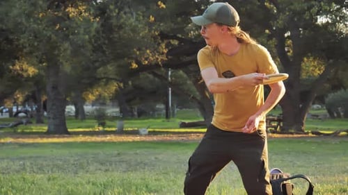 male with hat throws frisbee toward frisbee golf hole