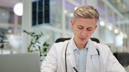 Male Doctor Working Diligently on Laptop and Taking Notes in a Modern Clinic