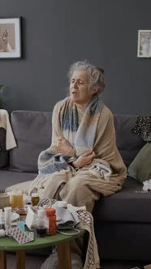 Senior Woman Sitting Sick on Couch with Blanket