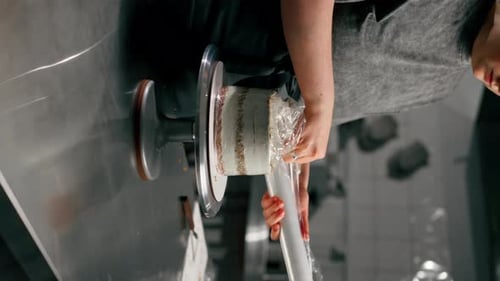 Vertical Video Female Baker in Professional Kitchen Wraps an Almost Finished Cake in Cling Film