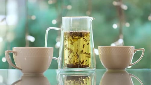 Teekanne mit Kräutertee und zwei weißen Tassen auf dem Tisch