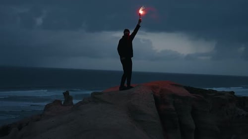 Man running up the coastline hill with red lit torch at dusk after sunset