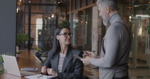 Cheerful Young Businesswoman Talking to Mature Man Waiter Making Order in Cafe