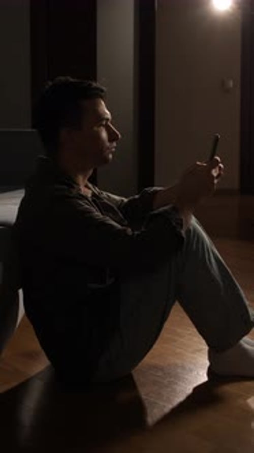 Vertical Video Man in Silhouette Sitting on Floor in Dark Apartment Late at Night Staring at