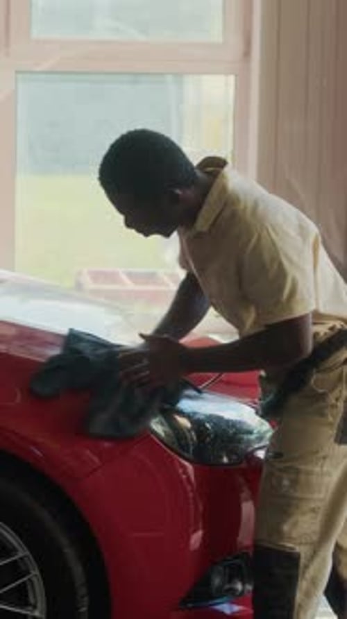 Vertical of African American Mechanic Polishing Red Car Hood with Cloth