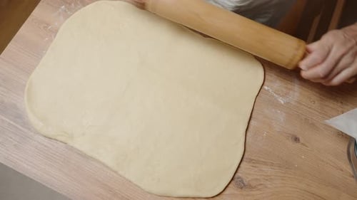 Flattening Dough into a Large Rectangle with a Wooden Rolling Pin, Ensuring Even Thickness.