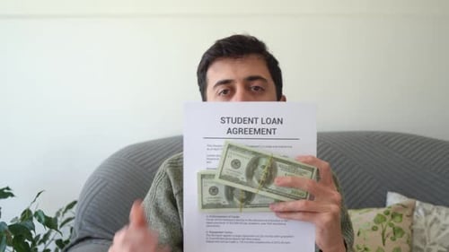 Man showing his student loan agreement and the cash he got with it. Concept of getting in debt to