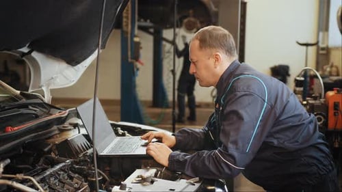 Confident Professional Car Mechanic Using a Computer Laptop to Diagnosing and