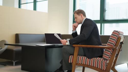 Un analyste, un professionnel, est assis à examiner attentivement les documents, travaillant seul dans un bureau moderne.