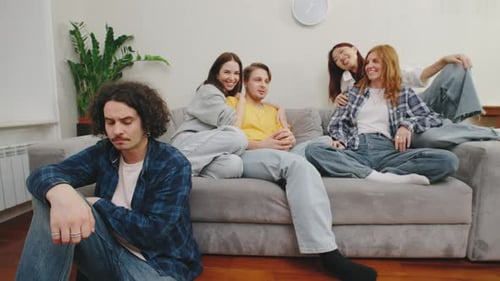 A Young Man Sits on the Floor Beside a Sofa Refusing to Engage with Two Couples Who Try to Talk to