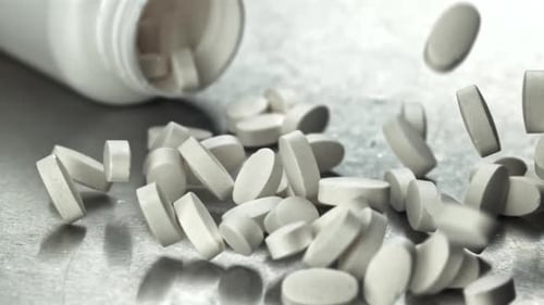 Des comprimés de médicaments blancs débordant sur une plate-forme réfléchissante filmés par une caméra haute vitesse à 1000 images par seconde