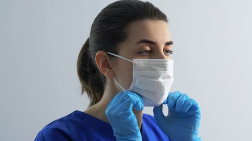 Woman in scrubs putting on protective face mask