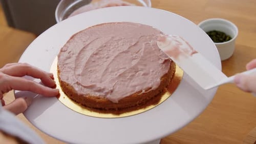 Young woman spreading creamy frosting on layer cake in her bright kitchen at home