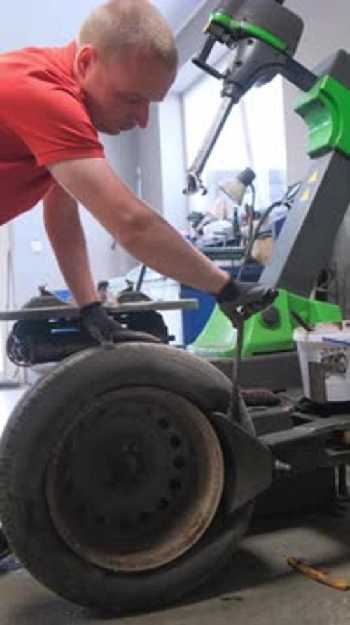Ein Automechaniker balanciert die Reifen des Autos: Das Konzept der Autoreparatur (Vertikales Video)