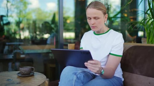 Woman Drinks Coffee Works on Tablet in Modern Cafe