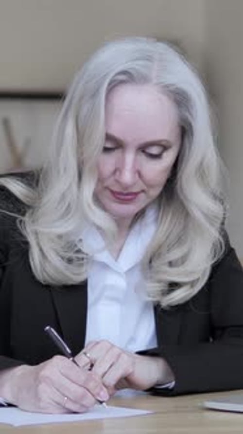 Mature Woman Writing on Paper at Her Desk