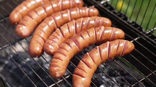 Sausages on a barbeque grill. Juicy sausages cooking over hot charcoal in smoke.