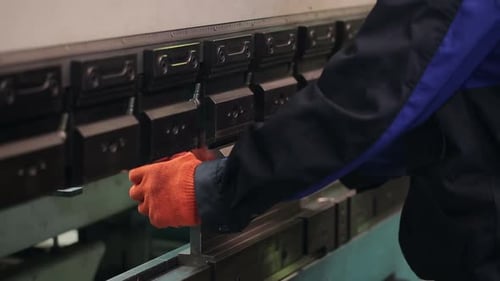 Techniker bei der Arbeit in einer modernen Anlage, Herstellung von Stahlteilen. Mann arbeitet mit Werkzeug in Handschuhen...