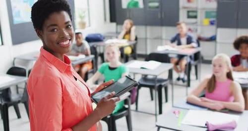 Portrait of diverse female teacher and happy schoolchildren at desks in school classroom