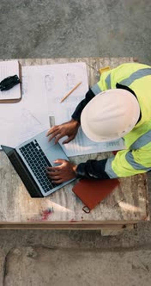 Blueprint, man and construction worker with laptop on site for planning home renovation from above