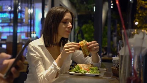 Young Woman Eating Tasty Meal in Cafe at Night 30s
