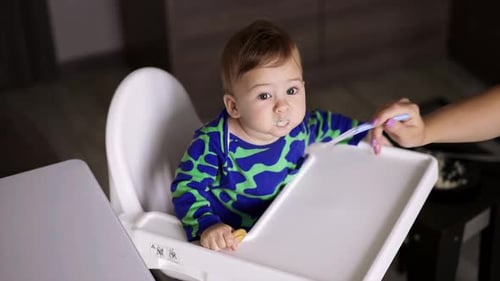 Cute little boy wearing blue and green shirt sitting at the feeding table.